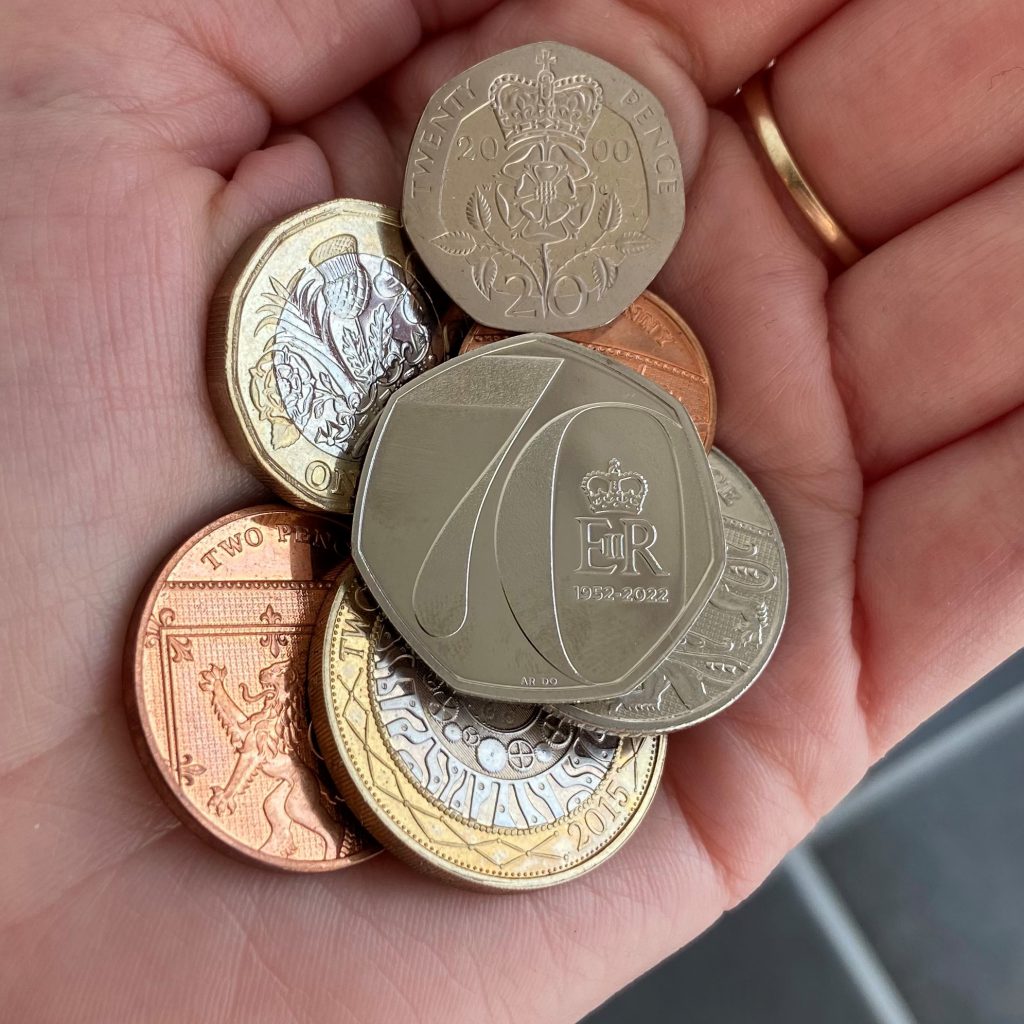 The 2022 Platinum Jubilee 50p enters circulation. 
Resting on top of a 10p, 2p, £2, £1, and 5p coin.
Coins are held in hand.